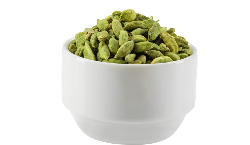Green cardamom pods in a bowl isolated on white background with copy space for text or images. Used as flavorings in both food and drink, as cooking spices and as a medicine. Frame composition, close-up shot.